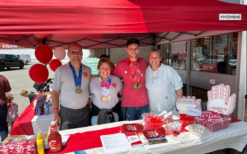 Diverse group of people standing under a red tent with Special Olympics materials in front of them